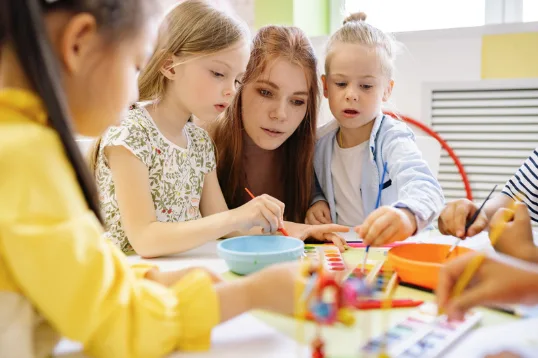 A group of children painting with a supporting adult