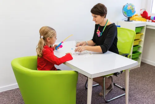 An occupational therapist and a young child playing a fine motor fishing game together at a table